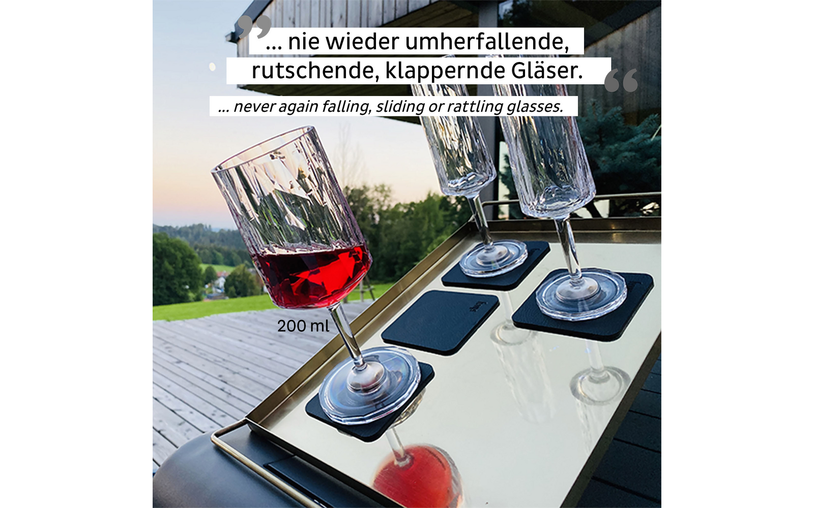 Three wine glasses with red wine on an illuminated wooden surface, garden landscape in the background