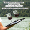 Two red wine glasses held on a metal plate by a hand outdoors over a lake