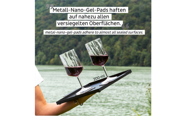 Two red wine glasses held on a metal plate by a hand outdoors over a lake