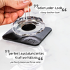 Hand holding a round transparent object above a black leather case with a hole