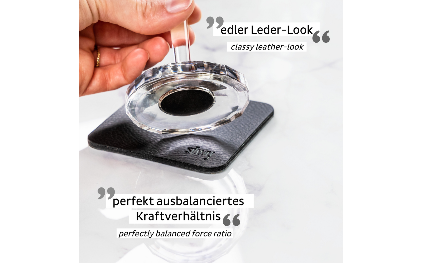 Hand holding a round transparent object above a black leather case with a hole