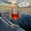 Wine glass with red drink on a boat at sunset over the water