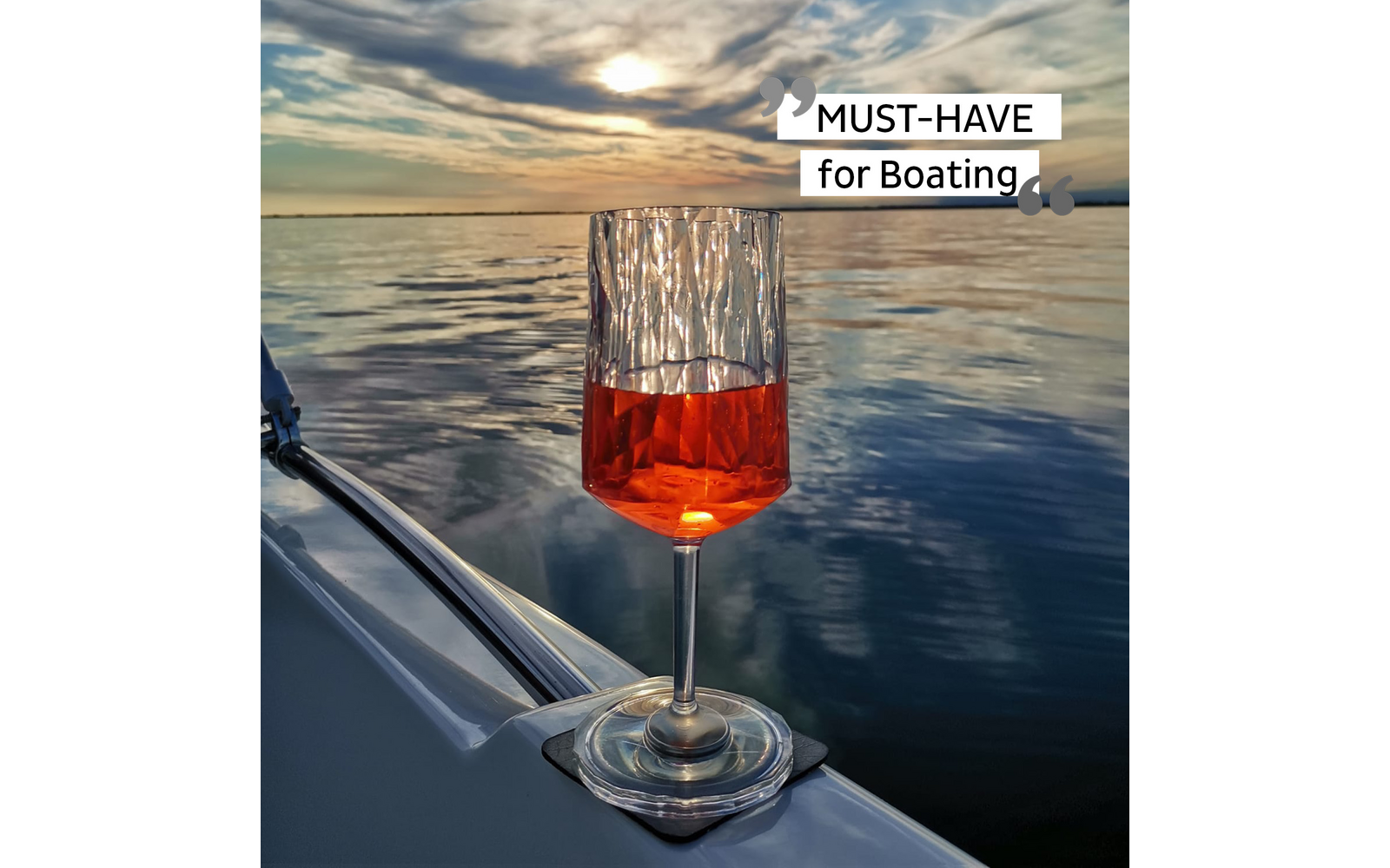 Wine glass with red drink on a boat at sunset over the water