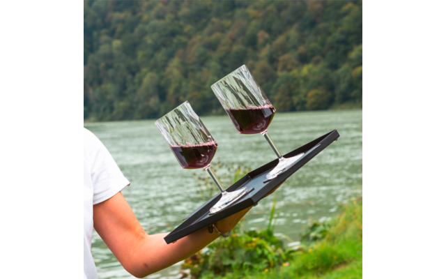 Person holding a tray with two glasses of red wine in front of a lake and forested hills