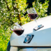 Two glasses of red wine are placed on the hood of a white car