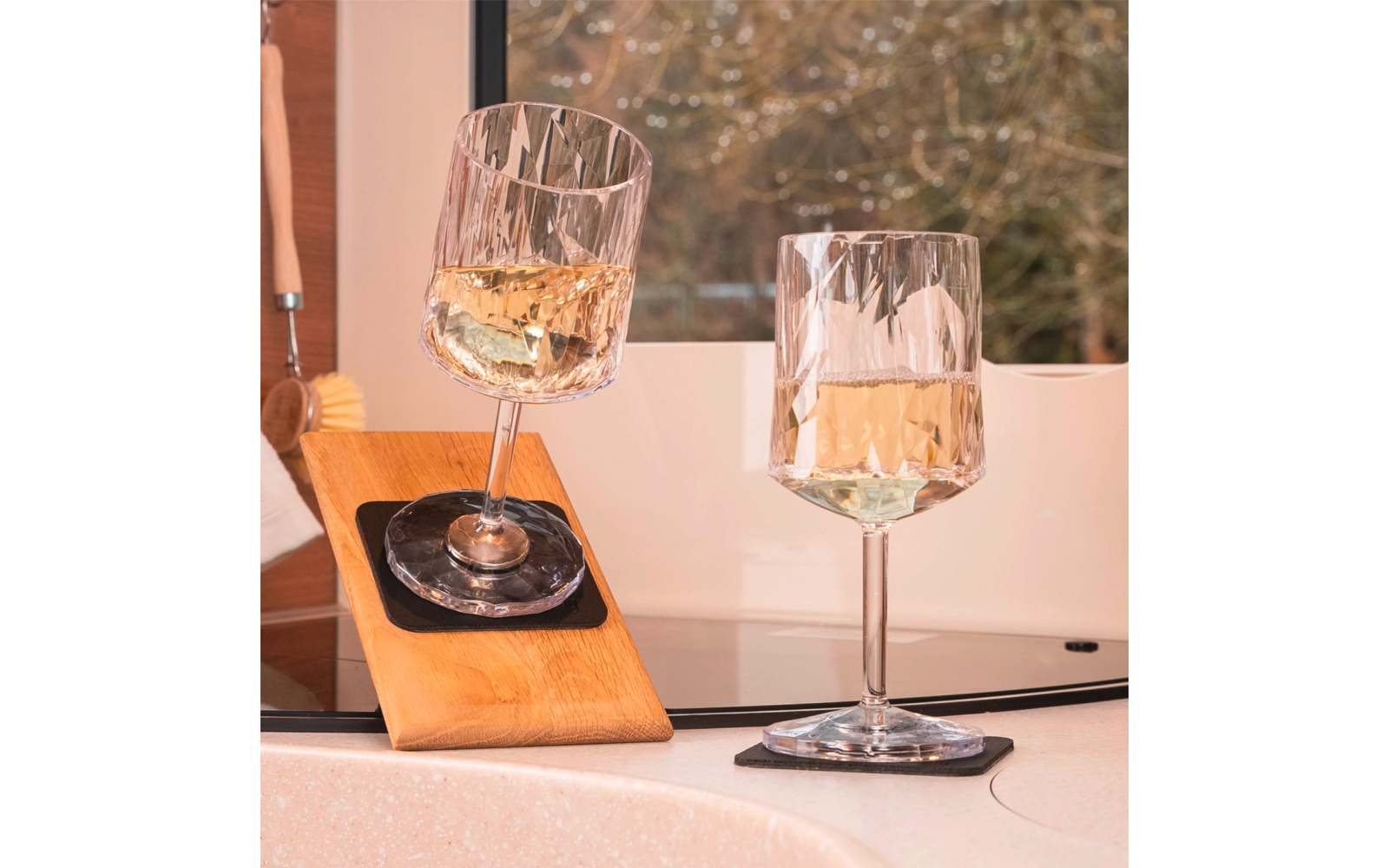 Two wine glasses with white wine on a light surface, blurred plants in the background