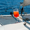 Glass with red drink on the netting of a sailboat, blue water surface in the background