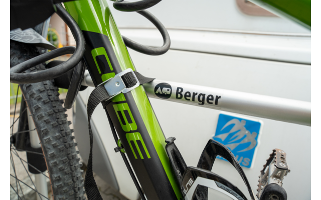 Tubo del telaio della bicicletta verde e nero con la scritta 'CUBE', tubo del telaio argentato con adesivo 'Berger', portaborraccia, pneumatico, pedale e lucchetto a cavo arrotolato