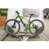 Mountain bike verde sul portapacchi posteriore di una roulotte bianca, gancio di traino e bordo stradale lastricato visibili