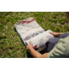Mains et avant-bras roulent un textile rectangulaire matelassé à motif géométrique sur l'herbe