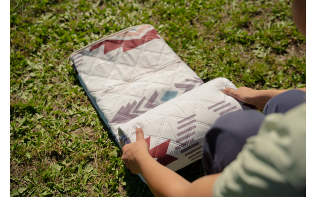 Mains et avant-bras roulent un textile rectangulaire matelassé à motif géométrique sur l'herbe