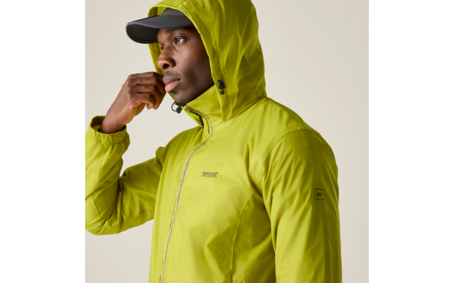 Person trägt eine limettengrüne Kapuzenjacke und eine schwarze Kappe, blickt nach links, Hand nahe am Gesicht, beiger Hintergrund