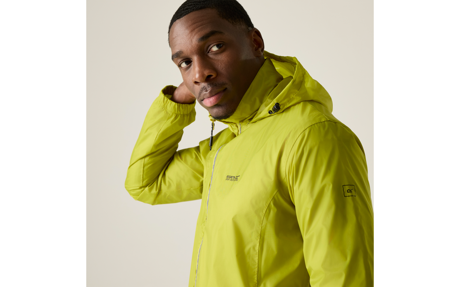 Person in hellgrüner Kapuzenjacke, eine Hand am Nacken, Blick zur Seite, heller einfarbiger Hintergrund