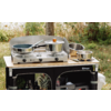 Réchaud à gaz deux feux avec casseroles et poêles sur une table de camping avec rangement, arbres et herbe en arrière-plan