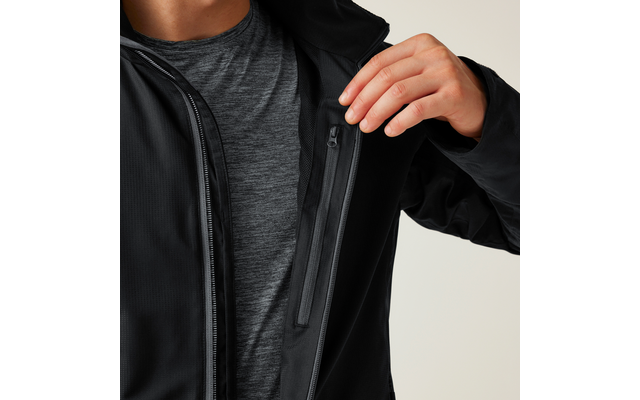 Nahaufnahme des Oberkörpers, eine Hand öffnet die Innentasche einer schwarzen Jacke, darunter ein graues T-Shirt