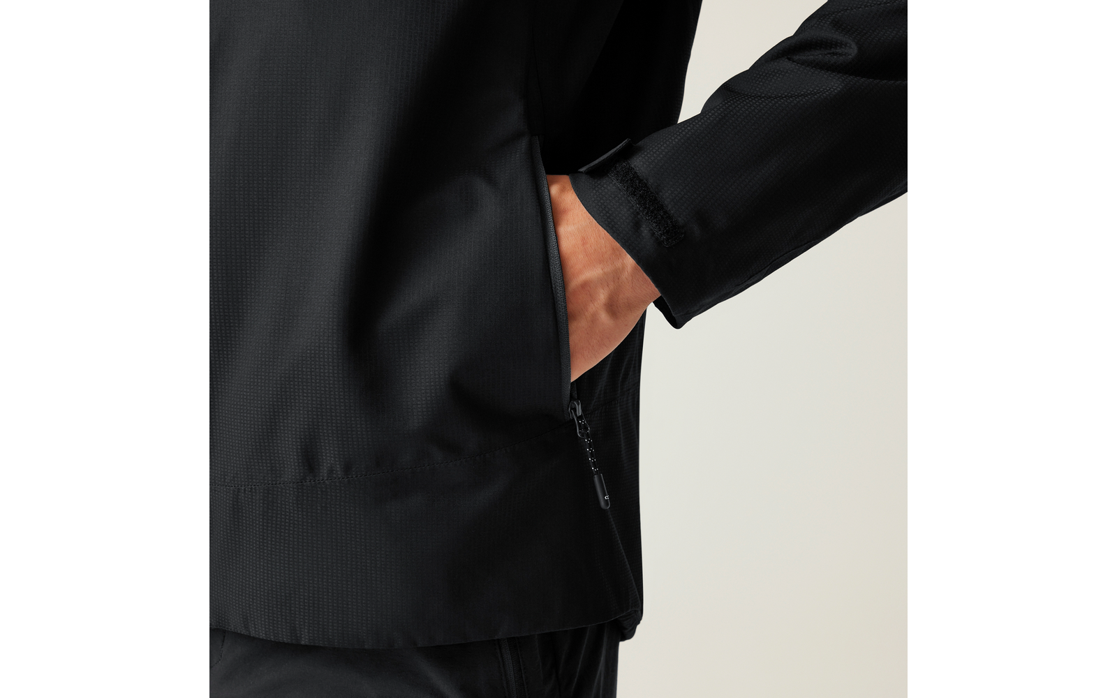 Nahaufnahme einer schwarzen Jacke, Hand steckt in einer seitlichen Reißverschlusstasche
