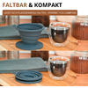 Sur une planche en bois une tasse en silicone pliable gris-bleu présentée dépliée et pliée, un verre double paroi contenant un liquide sombre, un tissu gris et deux bocaux en verre; en haut à gauche texte publicitaire 'FALT BAR & KOMPAKT' et 'LÄSST SICH PLATZSPAREND FALTEN – PERFEKT FÜR CAMPING'