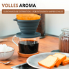 Porte-filtre à café pliable en silicone avec filtre en papier sur une tasse en verre de café noir sur une table en bois; sous-verre en liège, bocal de grains de café en arrière-plan, bocal de conservation à droite, assiette avec deux tranches de pâtisserie claire, petit bol avec morceaux de sucre, cuillère et smartphone; bandeau en haut VOLLES AROMA