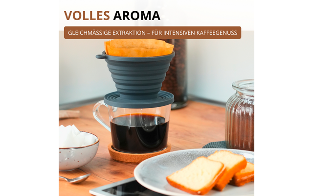 Porte-filtre à café pliable en silicone avec filtre en papier sur une tasse en verre de café noir sur une table en bois; sous-verre en liège, bocal de grains de café en arrière-plan, bocal de conservation à droite, assiette avec deux tranches de pâtisserie claire, petit bol avec morceaux de sucre, cuillère et smartphone; bandeau en haut VOLLES AROMA