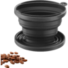 Objet rond noir en silicone pliable avec des anneaux concentriques et une petite boucle, à côté de grains de café bruns sur fond blanc