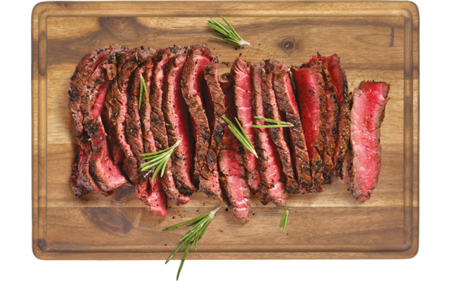 Aufgeschnittenes, gebratenes Steak auf einem Holzbrett mit grünen Kräutern