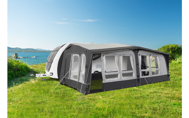 Caravan with attached awning on a green lawn near a lake under clear sky