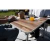 Holztisch mit 'Berger'-Logo, Glas Orangensaft, weiße Tasse, geflochtener Topf mit Pflanze, zwei Personen (nur Arme und Beine sichtbar), gemusterte Matte, Gras im Hintergrund