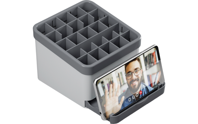 Ein graues Ladegerät mit mehreren Fächern und einem Smartphone, das ein Videotelefonat zeigt