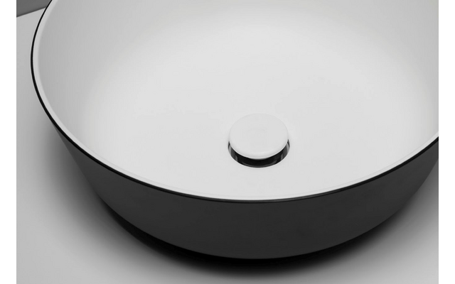 Lavabo redondo blanco con exterior negro y tapón de desagüe circular sobre fondo gris