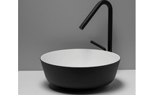 Vasque ronde à l'extérieur noire et intérieur blanc sur un plan clair; robinet noir haut avec bec courbé et levier; mur gris en arrière-plan