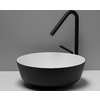 Lavabo rotondo con esterno nero e interno bianco su un piano chiaro; alto rubinetto nero con beccuccio curvo e leva; parete grigia sullo sfondo