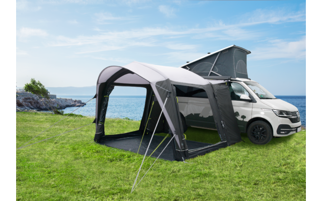 Furgoneta blanca con una extensión de tienda gris en un prado verde cerca de un lago