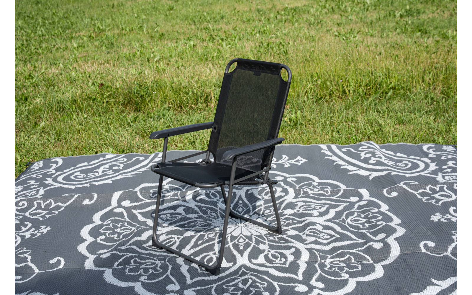 Zwarte stoel met metalen frame op een grijze mat met wit bloemmotief op gras