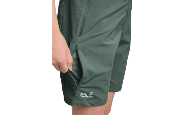 Main ouvrant une poche zippée sur un short vert foncé avec le logo Jack Wolfskin