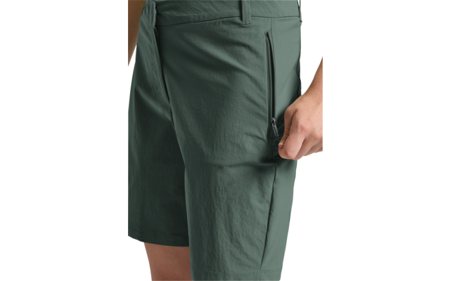 Bas du corps en short vert foncé, main droite tirant la fermeture éclair d'une poche latérale sur la cuisse