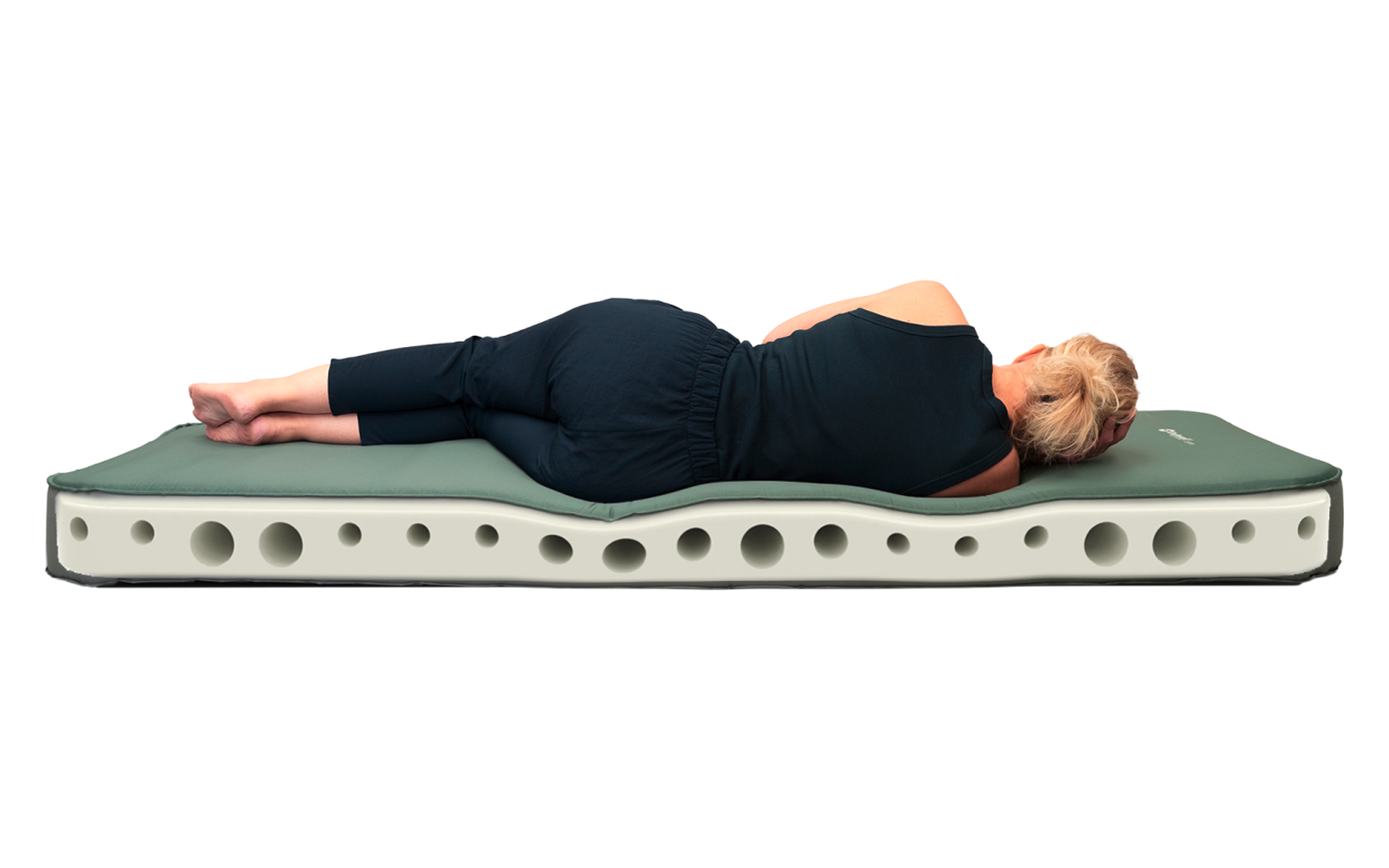 Person with short blond hair wearing a black top and black leggings lies on their side on a green pad on a white foam mattress with round holes