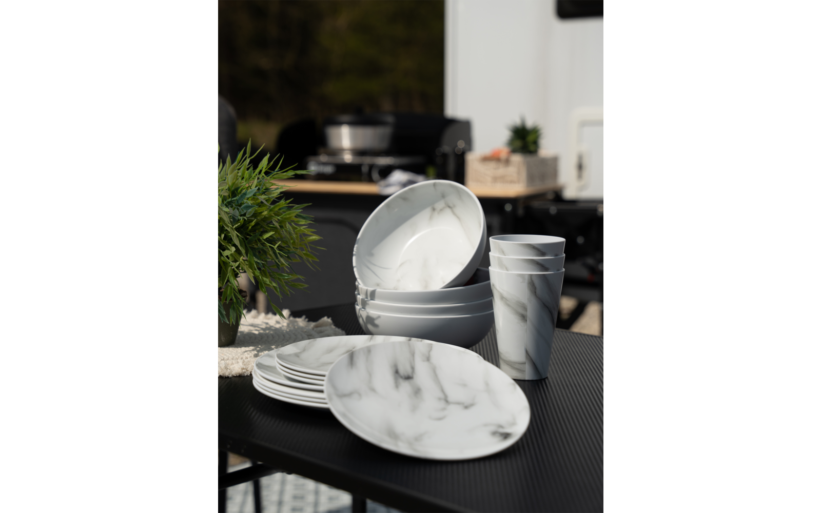 Mehrere weiße Geschirrteile mit grauem Marmor-Muster auf dunklem Tisch, im Hintergrund unscharfe grüne Pflanze