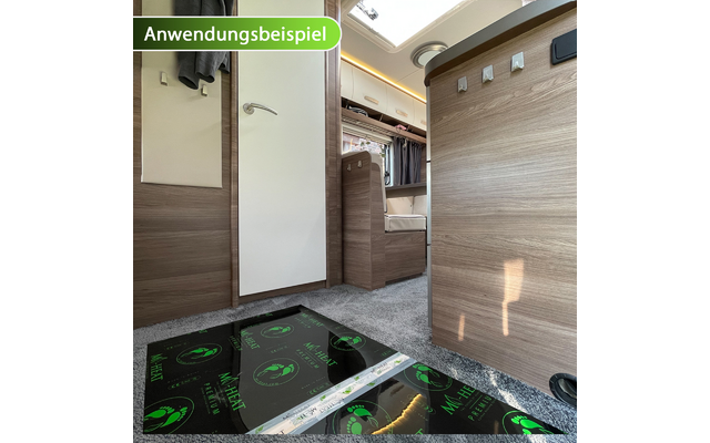 Innenraum eines Wohnmobils mit hellbraunen Holzfronten, grauem Teppichboden, weißer Tür, Sitzbank, Dachfenster und schwarzen glänzenden Heizfolien mit grünen Symbolen auf dem Boden; oben links grüner Schriftzug 'Anwendungsbeispiel'