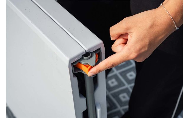 Main avec index appuyant sur un loquet en plastique orange dans une ouverture latérale d'un radiateur blanc; bracelet visible et sol à motif