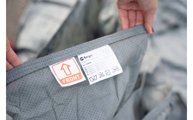 Twee handen houden grijze, gestippelde stof met een label 'FRONT' en een wasetiket met symbolen