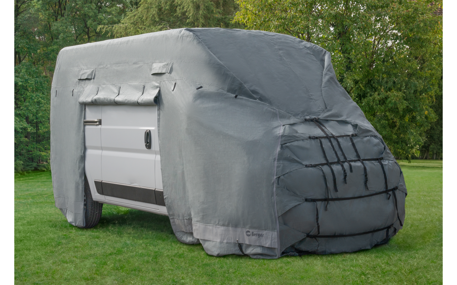 White van covered with a gray protective cover on grass, trees in the background