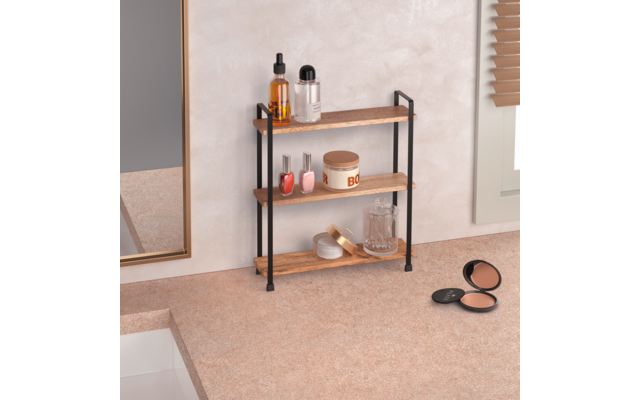 Dreistöckiges Holzregal mit schwarzem Metallgestell auf Arbeitsplatte neben Waschbecken; auf den Böden Flaschen, Nagellack, Cremedose, Seifenschale und Glas; Spiegelrahmen links, Jalousie rechts, geöffnetes Puderkompakt vorne