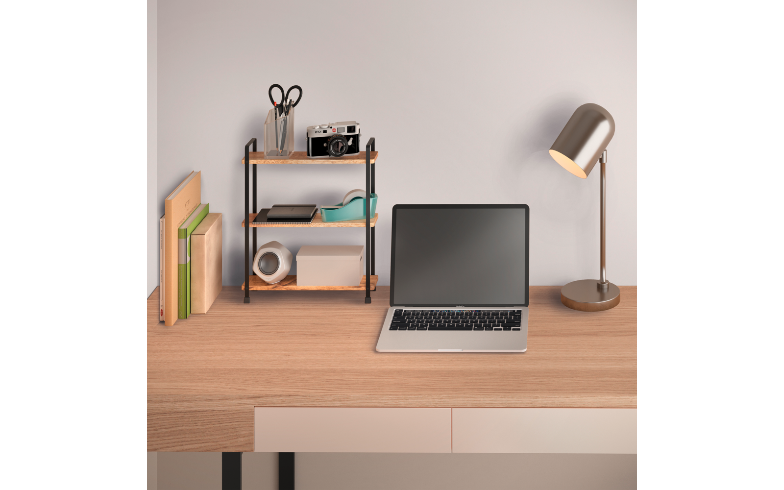 Holztisch mit offenem Laptop (schwarzer Bildschirm), rechts eine Metall-Schreibtischlampe, links ein kleines Regal mit Schere, Stifthalter, Kamera und Klebeband; Bücher und Ordner am linken Rand
