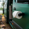 Witte toiletrol op houder bevestigd aan de open groene camperdeur; op de achtergrond bomen, een meer en een opvouwbare campingstoel
