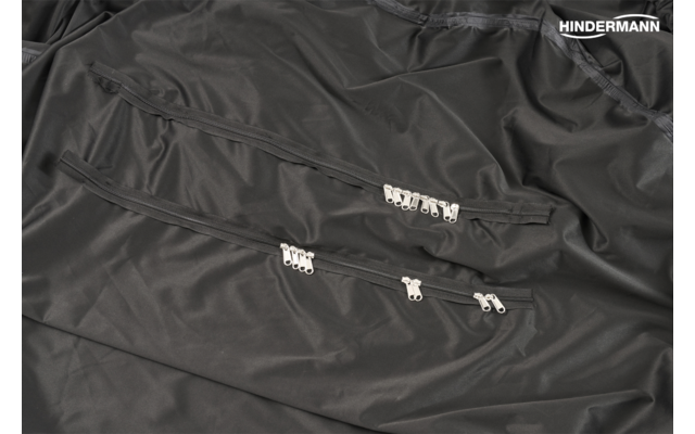 Schwarzer Stoff mit drei parallelen Reißverschlüssen und mehreren silbernen Zippern; weißes Logo "HINDERMANN" oben rechts
