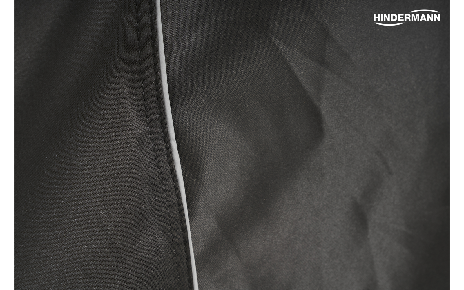 Schwarzer Stoff mit Naht und weißer Kante links, leichte Falten, Schriftzug 'HINDERMANN' oben rechts