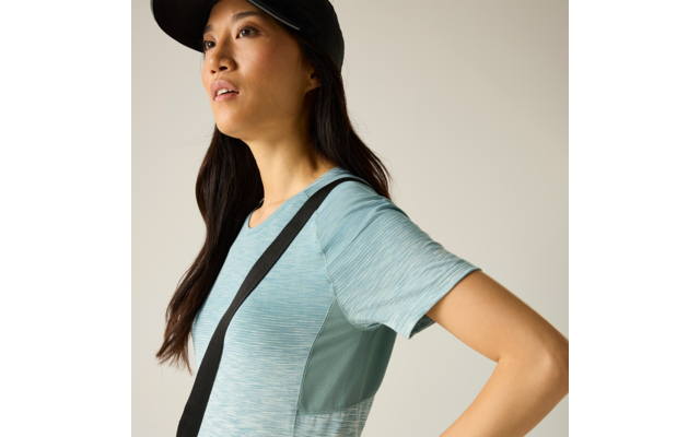 Plan rapproché latéral d'une personne portant une casquette noire, cheveux longs foncés, un haut de sport bleu clair à manches courtes et une lanière noire sur la poitrine ; regarde en haut à droite