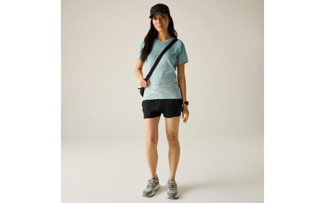 Personne debout sur fond clair, portant un t‑shirt vert menthe, un short noir, une casquette noire, des baskets grises, un sac bandoulière et une montre connectée