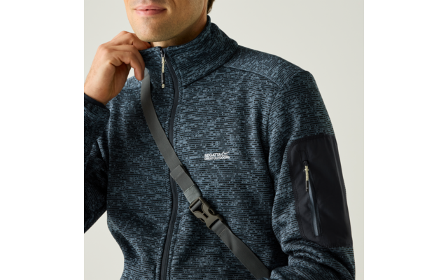 Nahaufnahme eines Mannes vom Kinn bis zum Oberkörper, er trägt eine dunkelblaue, gemusterte Fleecejacke mit Reißverschluss, einen Schultergurt über der Brust und eine Reißverschlusstasche am linken Oberarm