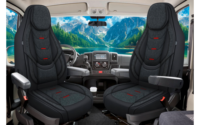 Zwei schwarze Vordersitze in einem Fahrzeugcockpit; Lenkrad, Armlehnen, Mittelkonsole mit Bedienelementen; durch die Windschutzscheibe sichtbare Berglandschaft und See